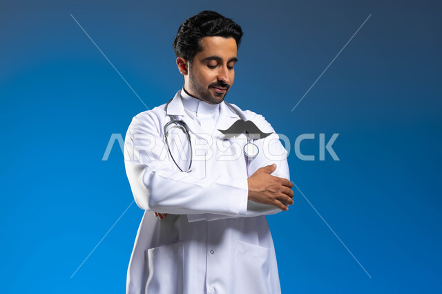 مفهوم مهنة الطب والعمل في القطاع الصحي، اليوم العالمي للرجل 19 نوفمبر، بورتريه مقرب لطبيب عربي خليجي سعودي يرتدي المعطف الطبي والسماعات الطبية يقف باستقامة وأيدي متقاطعة، النظر الى قصاصة ورقية على شكل شارب بايماءات الفخر، خلفية زرقاء