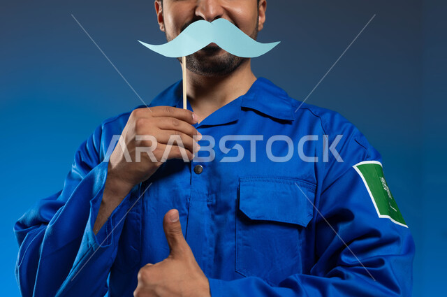 ايماءات الإعجاب والموافقة على شيء ما، اليوم العالمي للرجل 19 نوفمبر، الملاحة الجوية وهندسة الفضاء، بورتريه مقرب لرائد فضاء عربي خليجي سعودي يرتدي بدلة الفضاء الزرقاء بشعار علم السعودية يحمل بيده عود خشبي مع قصاصة ورقية على شكل شارب، خلفية زرقاء