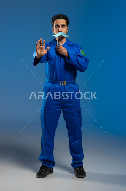 ايماءات يدين بمعنى قف واحذر، اليوم العالمي للرجل 19 نوفمبر، طلب التوقف والإبتعاد، مفهوم الملاحة الجوية وهندسة الفضاء، بورتريه مقرب لرائد فضاء عربي خليجي سعودي يرتدي بدلة الفضاء الزرقاء بشعار علم السعودية يحمل بيده عود خشبي مع قصاصة على شكل شارب، خلفية زرقاء