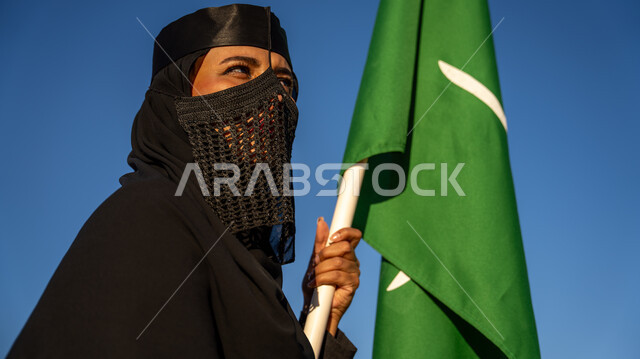 الفخر بالتراث السعودي, إظهار مشاعر الاعتزاز والتباهي بالهوية الوطنية, صورة مقربة لإمرأة عربية خليجية سعودية ترتدي البرقع والعباءة السوداء تمسك بيدها علم التأسيس باحترام, يوم بدينا 1727م, ذكرى تأسيس الدولة السعودية الأولى في 22 فبراير