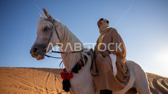 ارتداء الأزياء الشعبية في المناسبات الوطنية, توراث تربية الجياد من الأجداد, صورة من الجانب لفارس عربي خليجي سعودي يرتدي العقال الذهبي والبشت يمتطي فرس أبيض أصيل, التجول في الصحراء على ظهر الفرس, يوم بدينا 1727م, ذكرى تأسيس الدولة السعودية الأولى في 22 فبراير