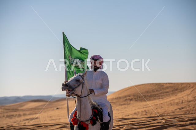 الفخر بالتراث السعودي الشعبي, فارس عربي خليجي سعودي يرتدي الثوب التقليدي والشماغ يمتطي فرس أبيض أصيل ويمسك بيده علم المملكة باعتزاز, يوم بدينا 1727م, تأسيس الدولة السعودية الأولى في 22 فبراير, احياء ذكرى اليوم الوطني في 23 سبتمبر, يوم العلم 11 مارس