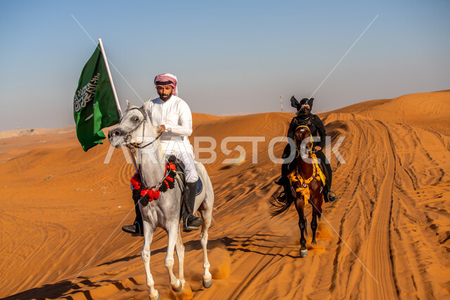 استذكار العيد الوطني في 23 سبتمبر, يوم بدينا 1727م, فارس وفارسة عربيان خليجيان سعوديان يتجولان على ظهر الفرس في الطبيعة الصحراوية, ذكرى تأسيس الدولة السعودية الأولى في 22 فبرير, رفع علم المملكة بفخر واعتزاز, الشغف بممارسة الهوايات الشعبية، يوم العلم 11 مارس