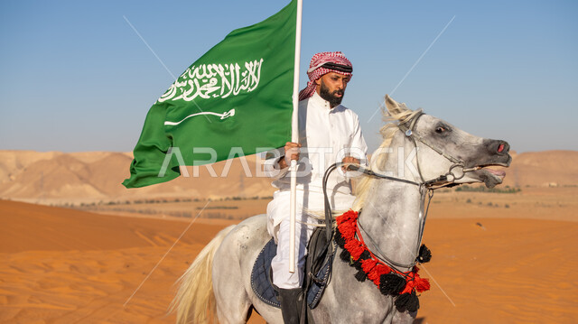الفخر بالتراث السعودي الشعبي, فارس عربي خليجي سعودي يرتدي الثوب التقليدي والشماغ يمتطي فرس أبيض أصيل ويمسك بيده علم المملكة باعتزاز, يوم بدينا 1727م, تأسيس الدولة السعودية الأولى في 22 فبراير, احياء ذكرى اليوم الوطني في 23 سبتمبر, يوم العلم 11 مارس