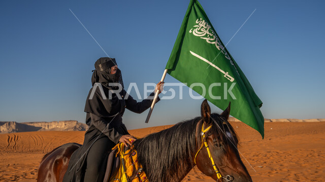 التجول في الصحراء على ظهر الفرس, صورة من الجانب لفارسة عربية خليجية سعودية ترتدي العباءة السوداء والبرقع تمتطي فرس بني أصيل, رفع علم المملكة بفخر واعتزاز في اليوم الوطني في 23 سبتمبر, يوم بدينا 1727م, ذكرى تأسيس الدولة السعودية الأولى في 22 فبراير