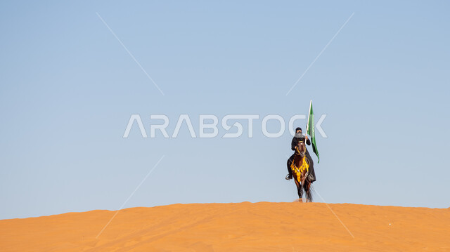 Our Day 1727 AD, remembering the National Day on September 23, the passion and passion for purebred horses, a Saudi Gulf Arab horsewoman wearing the burqa and black abaya, riding a purebred brown horse and holding the Kingdom’s flag proudly on Flag Day, March 11, the anniversary of the founding of the first Saudi state on February 22.