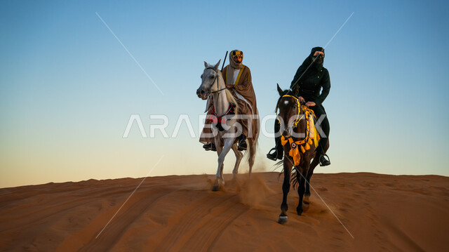 قوة وأصالة الحصان العربي، فعاليات وأنشطة ركوب الجياد العربية في الصحراء بمناسبة ذكرى تأسيس الدولة السعودية الأولى 22 فبراير، فارسان عربيان خليجيان سعوديان يرتديان الأزياء التقليدية الشعبية يمتطيان الخيول يتسابقان فوق الرمال الذهبية في النهار، يوم بدينا 1727 م