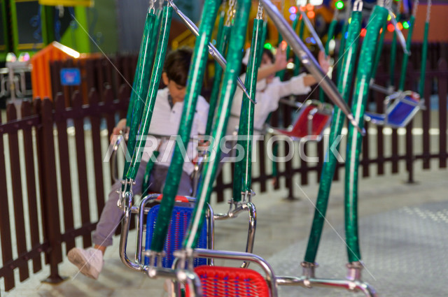 Two Saudi children in the amusement park, playing the fun game of swings, spending great times in the amusement park, electronic games, entertainment and entertainment, during the summer vacation