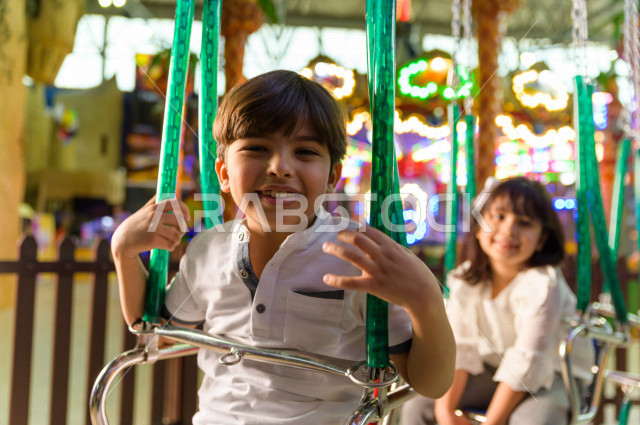 طفلان سعوديان في مدينة الألعاب ، يلعبان لعبة المراجيح المسلية  ، قضاء اوقات رائعة في مدينة الملاهي ، العاب الكترونية ، التسلية و الترفيه ، الترفيه في العطلة الصيفية
