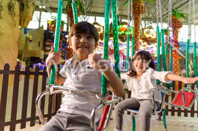 طفلان سعوديان في مدينة الألعاب ، يلعبان لعبة المراجيح المسلية  ، قضاء اوقات رائعة في مدينة الملاهي ، العاب الكترونية ، التسلية و الترفيه ، الترفيه في العطلة الصيفية