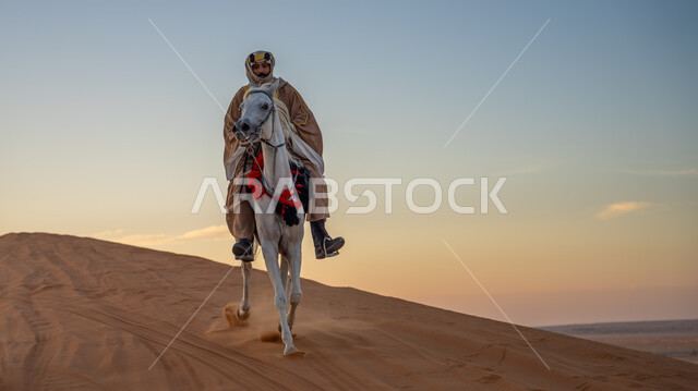 إحياء التراث الشعبي في تربية الجياد, ارتداء الأزياء الشعبية في ذكرى تأسيس الدولة السعودية الأولى في 22 فبراير, يوم بدينا 1727م, مفهوم العناية بالأحصنة في المملكة, فارس عربي خليجي سعودي يرتدي البشت والعقال الذهبي يمتطي فرس أبيض أصيل ويتجول في المناطق الصحراوية
