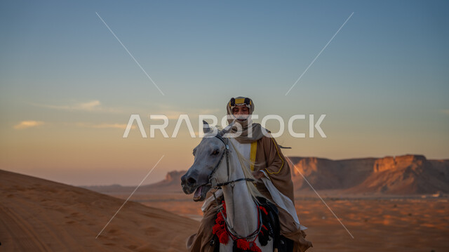ارتداء الأزياء الشعبية في ذكرى تأسيس الدولة السعودية الأولى في 22 فبراير, يوم بدينا 1727م, مفهوم العناية بالأحصنة في المملكة, إحياء التراث الشعبي في تربية الجياد, فارس عربي خليجي سعودي يرتدي البشت والعقال الذهبي يمتطي فرس أبيض أصيل ويتجول في المناطق الصحراوية