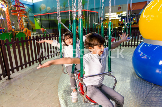 Two Saudi children in the amusement park, playing the fun game of swings, spending great times in the amusement park, electronic games, entertainment and entertainment, during the summer vacation