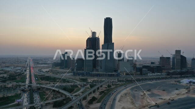 تحقيق النهضة الاقتصادية والتجارية, الاشجار والنباتات الخضراء, النمو والتطور الهندسي المعماري للأبراج وناطحات السحاب بالسعودية، حركة سير السيارات على الطريق العام وقت الغروب،  بناء مستقبل حضاري ومتطور، مركز الملك عبدالله المالي(كافد) في الرياض