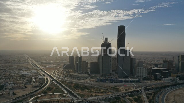 مركز الملك عبدالله المالي ( كافد )، الأماكن والمعالم المشهورة, الفن الهندسي المعماري للمباني والمنشآت الاقتصادية, منظر السماء المليئة بالغيوم فوق الأبراج وناطحات السحاب وقت غروب الشمس, النمو والتطور العمراني, الحركة المرورية للسيارات في طرق شوارع مدينة الرياض