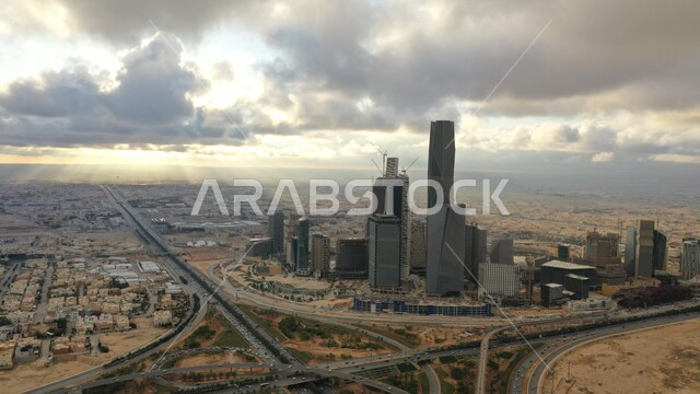 أماكن ومعالم مشهورة في الرياض، الفن الهندسي المعماري للمباني وناطحات السحاب والأبراج في السعودية وقت الغروب, النمو والتطورالعمراني, صورة للسماء المليئة بالغيوم البيضاء فوق مدينة الملك عبدالله المالي (كافد), حركة سير السيارات في الطرق والشوارع المتطورة
