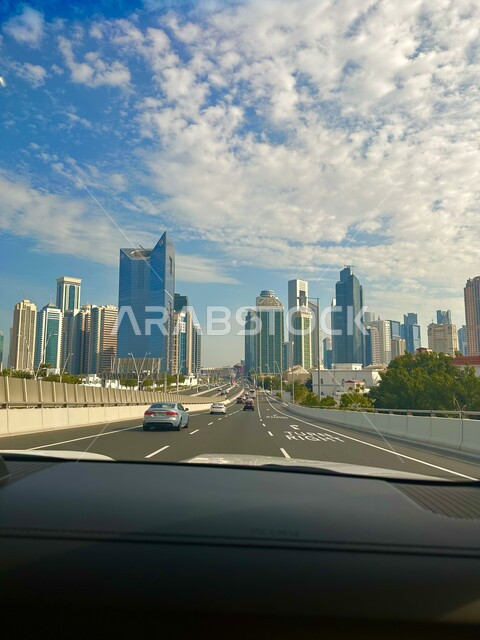 الحركة المرورية للسيارت داخل العاصمة، منظر الغيوم البيضاء في السماء فوق الأبراج وناطحات السحاب في النهار، الاهتمام بزراعة الأشجار والنباتات الخضراء في الطرقات العامة، صورة من داخل السيارة لخط السير السريع والشوارع الاسفلتيه المعبدة في مدينة الدوحة
