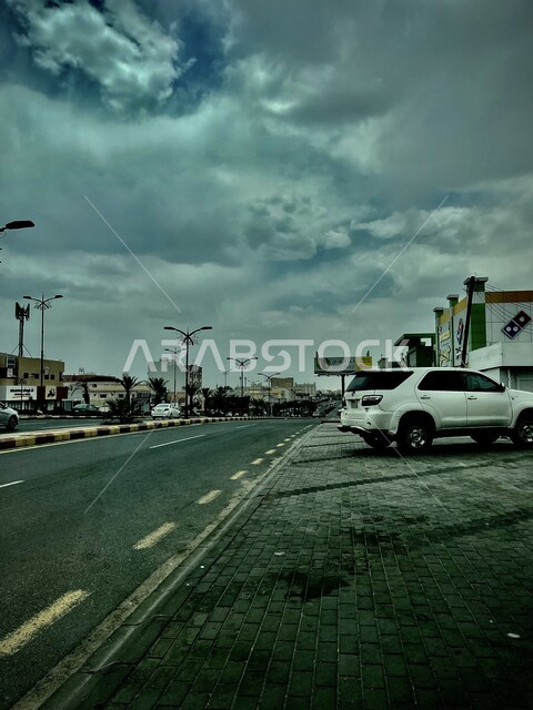 منظر السماء المليئة بالغيوم البيضاء في الأجواء الضبابية، اعمدة الانارة في شوارع المملكة العربية السعودية، طريق اسفلتي معبد، البيوت والمباني السكنية، الأرصفة والطرقات المهيئة والمعبدة في المدينة
