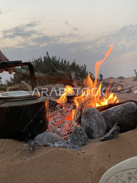 الاستمتاع بالمشروبات الساخنة في الأجواء الشتوية الباردة، صورة مقربة لإبريق شاي على نار الحطب المشتعلة، كرم الضيافه وحسن الاستقبال، متعة احتساء الشاي في الكشتات البرية العربية الشعبية، أجواء التخييم في المناطق الصحراوية في المملكة العربية السعودية