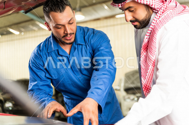 رجل عربي سعودي  داخل ورشة السيارات  ، بصحبة مهندس ميكانيكي يقوم باصلاح سيارته ، استخدام ادوات للصيانة ، اصلاح يدوي ، خدمات اصلاح و صيانة السيارات ، مهندس ميكانيكي ، ورشة صيانة 