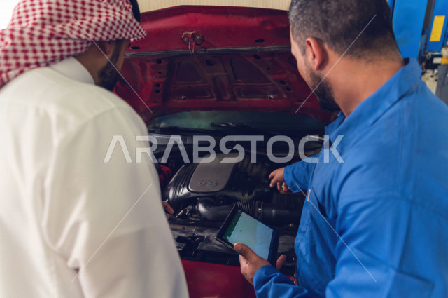 رجل عربي سعودي  داخل ورشة السيارات  ، بصحبة مهندس ميكانيكي يقوم باصلاح سيارته ، استخدام ادوات للصيانة ، اصلاح يدوي ، خدمات اصلاح و صيانة السيارات ، مهندس ميكانيكي ، ورشة صيانة 