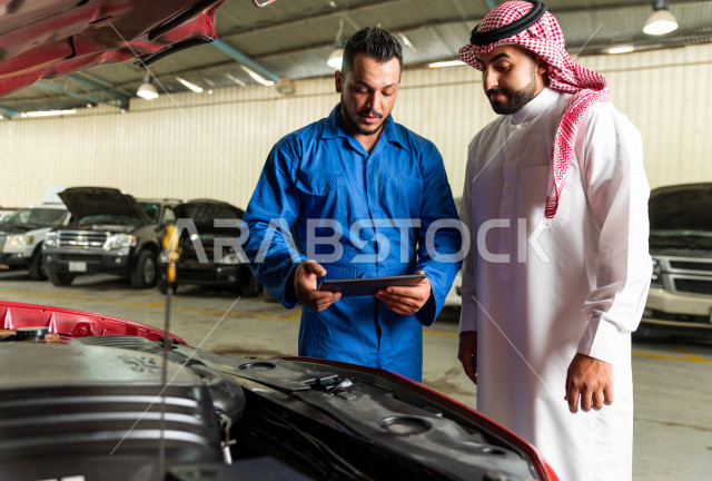 رجل عربي سعودي  داخل ورشة السيارات  ، بصحبة مهندس ميكانيكي يقوم باصلاح سيارته ، استخدام ادوات للصيانة ، اصلاح يدوي ، خدمات اصلاح و صيانة السيارات ، مهندس ميكانيكي ، ورشة صيانة 