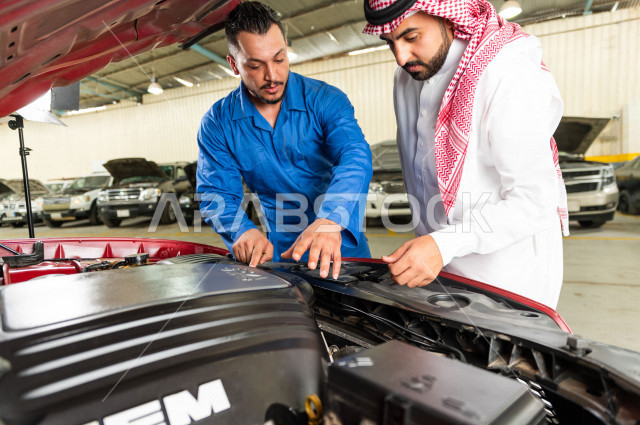 رجل عربي سعودي  داخل ورشة السيارات  ، بصحبة مهندس ميكانيكي يقوم باصلاح سيارته ، استخدام ادوات للصيانة ، اصلاح يدوي ، خدمات اصلاح و صيانة السيارات ، مهندس ميكانيكي ، ورشة صيانة 