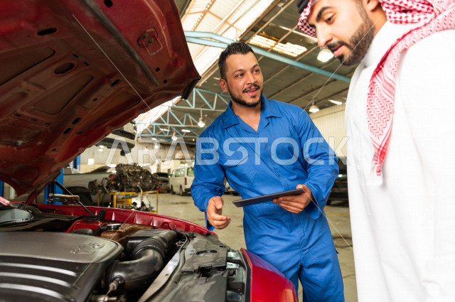 رجل عربي سعودي  داخل ورشة السيارات  ، بصحبة مهندس ميكانيكي يقوم باصلاح سيارته ، استخدام ادوات للصيانة ، اصلاح يدوي ، خدمات اصلاح و صيانة السيارات ، مهندس ميكانيكي ، ورشة صيانة 