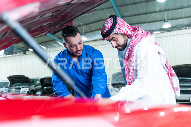 رجل عربي سعودي  داخل ورشة السيارات  ، بصحبة مهندس ميكانيكي يقوم باصلاح سيارته ، استخدام ادوات للصيانة ، اصلاح يدوي ، خدمات اصلاح و صيانة السيارات ، مهندس ميكانيكي ، ورشة صيانة 