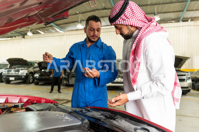 رجل عربي سعودي  داخل ورشة السيارات  ، بصحبة مهندس ميكانيكي يقوم باصلاح سيارته ، استخدام ادوات للصيانة ، اصلاح يدوي ، خدمات اصلاح و صيانة السيارات ، مهندس ميكانيكي ، ورشة صيانة 