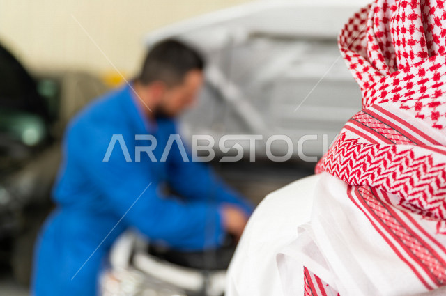 رجل عربي سعودي  داخل ورشة السيارات  ، بصحبة مهندس ميكانيكي يقوم باصلاح سيارته ، استخدام ادوات للصيانة ، اصلاح يدوي ، خدمات اصلاح و صيانة السيارات ، مهندس ميكانيكي ، ورشة صيانة 