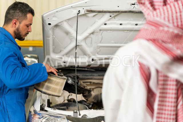 رجل عربي سعودي  داخل ورشة السيارات  ، بصحبة مهندس ميكانيكي يقوم باصلاح سيارته ، استخدام ادوات للصيانة ، اصلاح يدوي ، خدمات اصلاح و صيانة السيارات ، مهندس ميكانيكي ، ورشة صيانة 