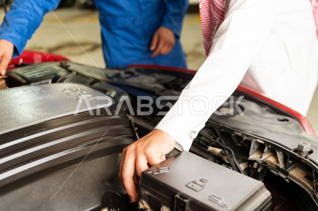 رجل عربي سعودي  داخل ورشة السيارات  ، بصحبة مهندس ميكانيكي يقوم باصلاح سيارته ، استخدام ادوات للصيانة ، اصلاح يدوي ، خدمات اصلاح و صيانة السيارات ، مهندس ميكانيكي ، ورشة صيانة 