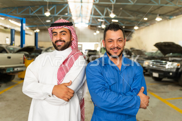 رجل  عربي سعودي يقف مع المهندس الميكانيكي داخل ورشة السيارات  ، بايماءات وجه و يدين مختلفة  ، خدمات اصلاح و صيانة السيارات ، مهندس ميكانيكي ، ورشة صيانة 