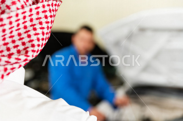 رجل عربي سعودي  داخل ورشة السيارات  ، بصحبة مهندس ميكانيكي يقوم باصلاح سيارته ، استخدام ادوات للصيانة ، اصلاح يدوي ، خدمات اصلاح و صيانة السيارات ، مهندس ميكانيكي ، ورشة صيانة 