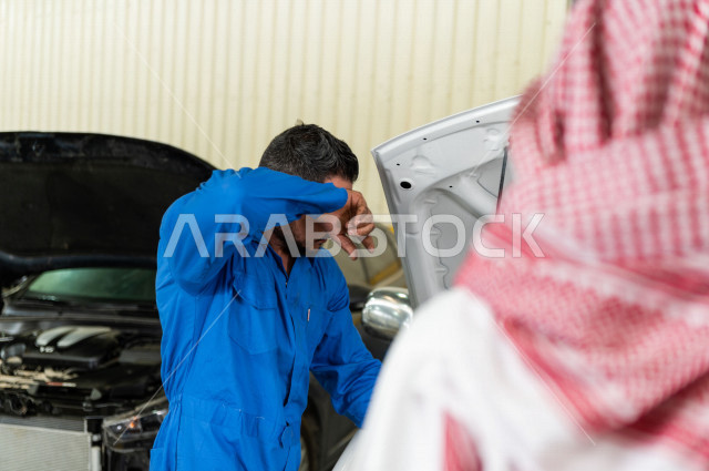 رجل عربي سعودي  داخل ورشة السيارات  ، بصحبة مهندس ميكانيكي يقوم باصلاح سيارته ، استخدام ادوات للصيانة ، اصلاح يدوي ، خدمات اصلاح و صيانة السيارات ، مهندس ميكانيكي ، ورشة صيانة 