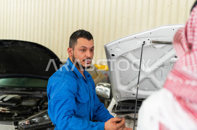 رجل عربي سعودي  داخل ورشة السيارات  ، بصحبة مهندس ميكانيكي يقوم باصلاح سيارته ، استخدام ادوات للصيانة ، اصلاح يدوي ، خدمات اصلاح و صيانة السيارات ، مهندس ميكانيكي ، ورشة صيانة 