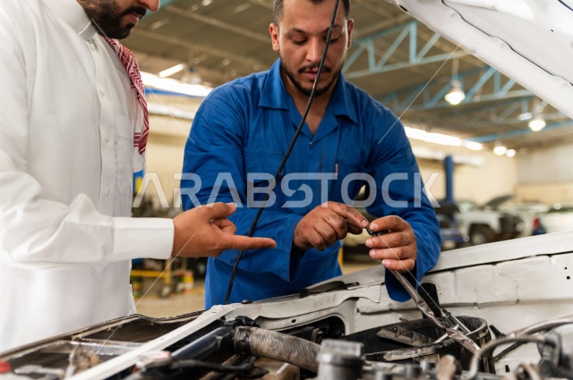 رجل عربي سعودي  داخل ورشة السيارات  ، بصحبة مهندس ميكانيكي يقوم باصلاح سيارته ، استخدام ادوات للصيانة ، اصلاح يدوي ، خدمات اصلاح و صيانة السيارات ، مهندس ميكانيكي ، ورشة صيانة 