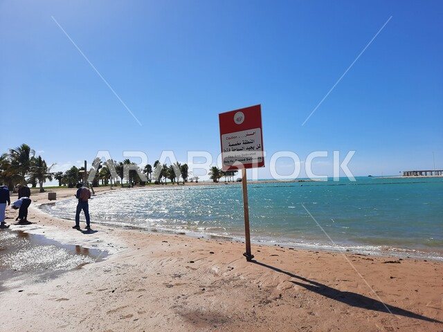 لافتات التنبيه والتحذير على شاطئ الهيئة الملكية في منطقة الجار في النهار، زراعة أشجار النخيل والنباتات الخضراء في المدن السياحية، مناطق وأماكن طبيعية عائليه ترفيهيه على ساحل البحر الاحمر، السواحل الشاطئية والواجهة البحرية في مدينة ينبع في المملكة العربية السعودية