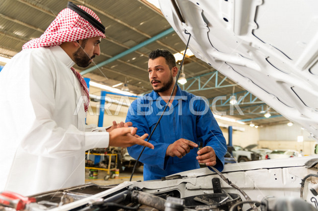 رجل عربي سعودي  داخل ورشة السيارات  ، بصحبة مهندس ميكانيكي يقوم باصلاح سيارته ، استخدام ادوات للصيانة ، اصلاح يدوي ، خدمات اصلاح و صيانة السيارات ، مهندس ميكانيكي ، ورشة صيانة 