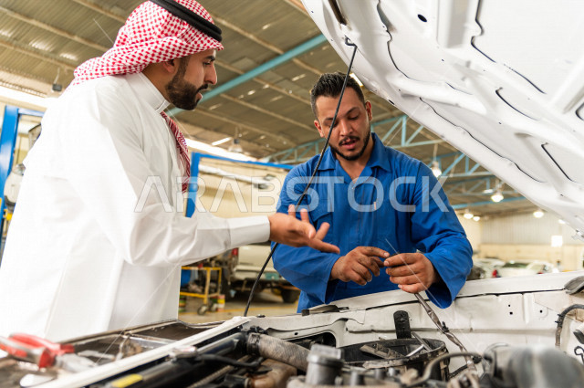 رجل عربي سعودي  داخل ورشة السيارات  ، بصحبة مهندس ميكانيكي يقوم باصلاح سيارته ، استخدام ادوات للصيانة ، اصلاح يدوي ، خدمات اصلاح و صيانة السيارات ، مهندس ميكانيكي ، ورشة صيانة 