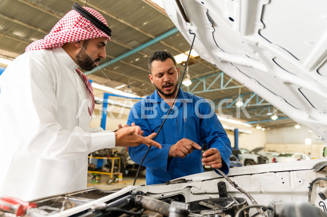 رجل عربي سعودي  داخل ورشة السيارات  ، بصحبة مهندس ميكانيكي يقوم باصلاح سيارته ، استخدام ادوات للصيانة ، اصلاح يدوي ، خدمات اصلاح و صيانة السيارات ، مهندس ميكانيكي ، ورشة صيانة 