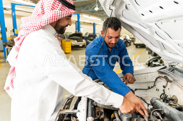 رجل عربي سعودي  داخل ورشة السيارات  ، بصحبة مهندس ميكانيكي يقوم باصلاح سيارته ، استخدام ادوات للصيانة ، اصلاح يدوي ، خدمات اصلاح و صيانة السيارات ، مهندس ميكانيكي ، ورشة صيانة 