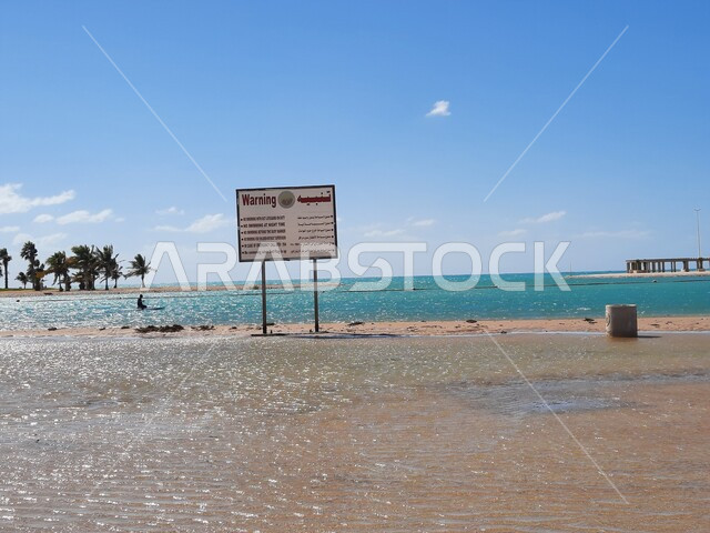 لافتات التنبيه والتحذير على شاطئ الهيئة الملكية في منطقة الجار في النهار، زراعة أشجار النخيل والنباتات الخضراء في المدن السياحية، مناطق وأماكن طبيعية عائليه ترفيهيه على ساحل البحر الاحمر، السواحل الشاطئية والواجهة البحرية في مدينة ينبع في المملكة العربية السعودية