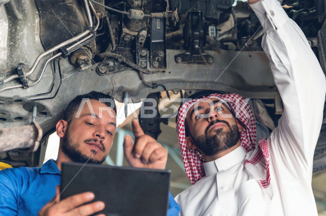 رجل عربي سعودي  داخل ورشة السيارات ، يستخدم جهاز التابلت لاختيار خدمة التصليح ، معه مهندس ميكانيكي يقوم باصلاح سيارته ، استخدام ادوات للصيانة ، اصلاح يدوي ، خدمات اصلاح و صيانة السيارات ، مهندس ميكانيكي ، ورشة صيانة 