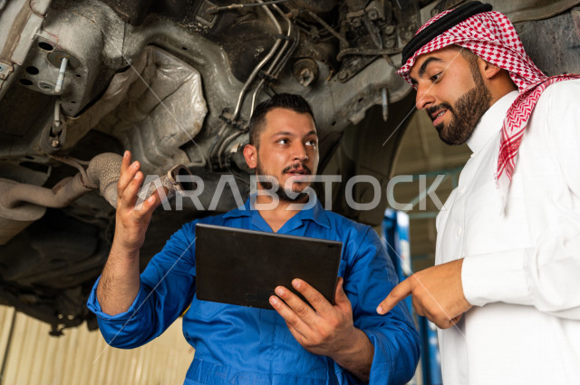 رجل عربي سعودي  داخل ورشة السيارات ، يستخدم جهاز التابلت لاختيار خدمة التصليح ، معه مهندس ميكانيكي يقوم باصلاح سيارته ، استخدام ادوات للصيانة ، اصلاح يدوي ، خدمات اصلاح و صيانة السيارات ، مهندس ميكانيكي ، ورشة صيانة 