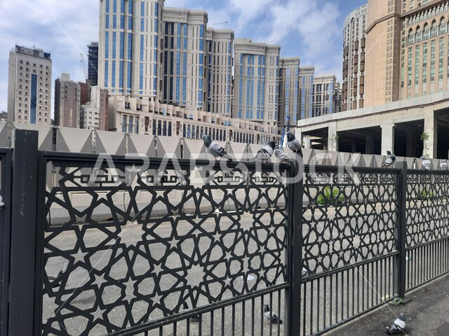 الفن الهندسي المعماري للأبراج بالقرب من المسجد الحرام في مكة المكرمه، مدن ومعالم إسلامية دينية مقدسة، صورة مقربة لسور معدني اسود مزخرف بكلمة مكه  في موقف كدي لحافلات الحرم المكي