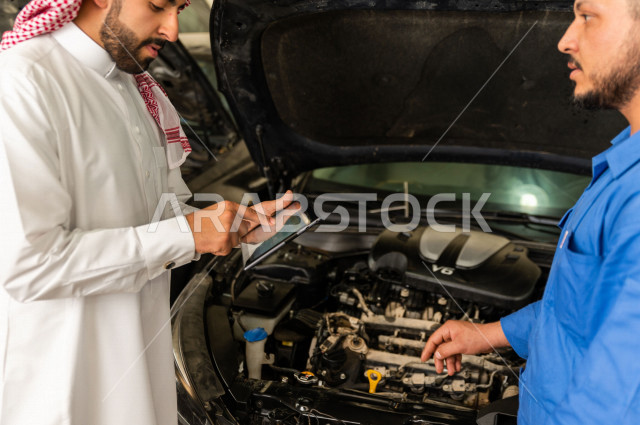 رجل عربي سعودي  داخل ورشة السيارات ، يستخدم جهاز التابلت لاختيار خدمة التصليح ، معه مهندس ميكانيكي يقوم باصلاح سيارته ، استخدام ادوات للصيانة ، اصلاح يدوي ، خدمات اصلاح و صيانة السيارات ، مهندس ميكانيكي ، ورشة صيانة 