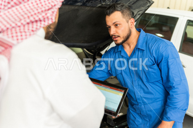 رجل عربي سعودي  داخل ورشة السيارات ، يستخدم جهاز التابلت لاختيار خدمة التصليح ، معه مهندس ميكانيكي يقوم باصلاح سيارته ، استخدام ادوات للصيانة ، اصلاح يدوي ، خدمات اصلاح و صيانة السيارات ، مهندس ميكانيكي ، ورشة صيانة 