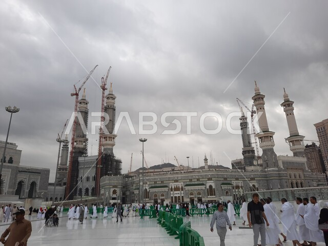 تجمع الحجاج والمعتمرين في الساحة الخارجية لمسجد الله الحرام في مكة مكرمة، مقاصد واماكن لأداء العبادات والتقرب الى الله, معالم دينية اسلامية مقدسة في المملكة العربية السعودية، الأجواء الغائمة ومشهد السماء المليئة بالغيوم السوداء